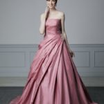 Vestido de novia de color en satèn, el busto semirrígido y preformado está enriquecido con encaje, la falda drapeada en diagonal tiene una decoración en el lateral de lentejuelas y piedras brillantes
