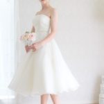 Abito da sposa corto semplice liscio fatto in organza e raso con scollo dritto e reggiseno interno, gonna ampia con importante cintura gioiello in vita.