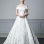 Unconventional satin wedding dress with semi-rigid and preformed bustier, skirt embellished with a large fabric flower on the back and organza ruffles