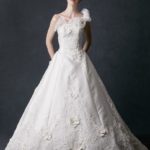 Original and extravagant one-shoulder wedding dress made in satin embellished with lace embroidery, sequins, rhinestones and floral fabric decorations