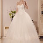 Abito da sposa in stile principesco realizzato in raso e tulle decorato da pizzo e perline, bustino stretto finemente impreziosito e gonna ampia a balze